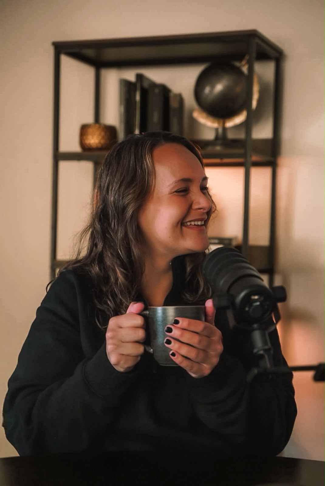 Mariah laughing in the studio, holding a mug beside a microphone